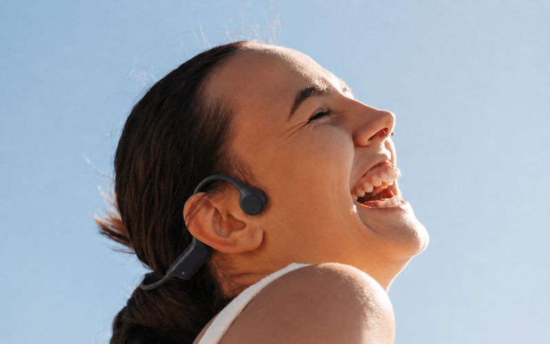 Mujer sonriente al sol con audifonos OSSonic