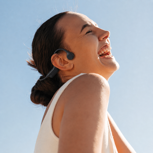 Mujer sonriente al sol con audifonos OSSonic